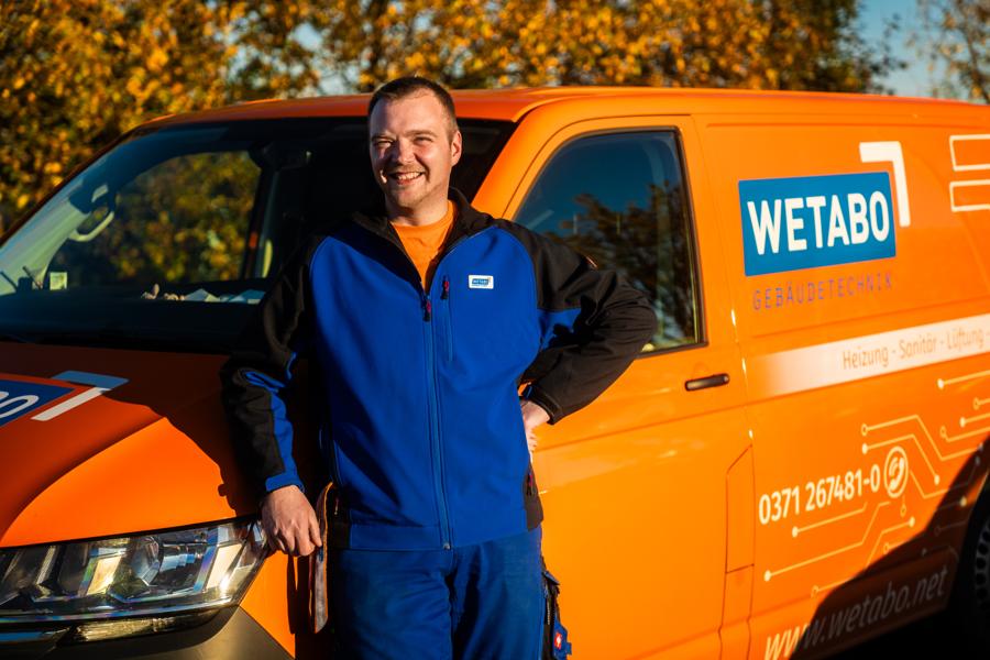 WETABO-Monteur lehnt am orangen Firmentransporter
